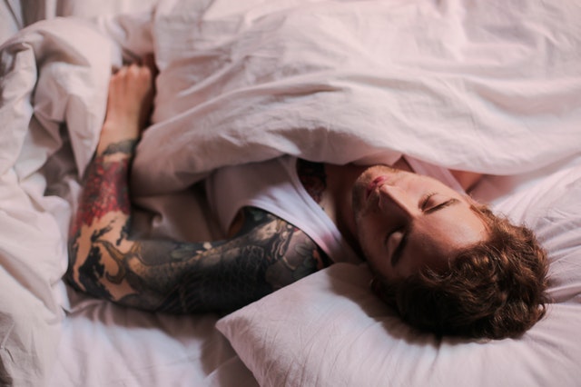 man with tattoos sleeping in a white shirt