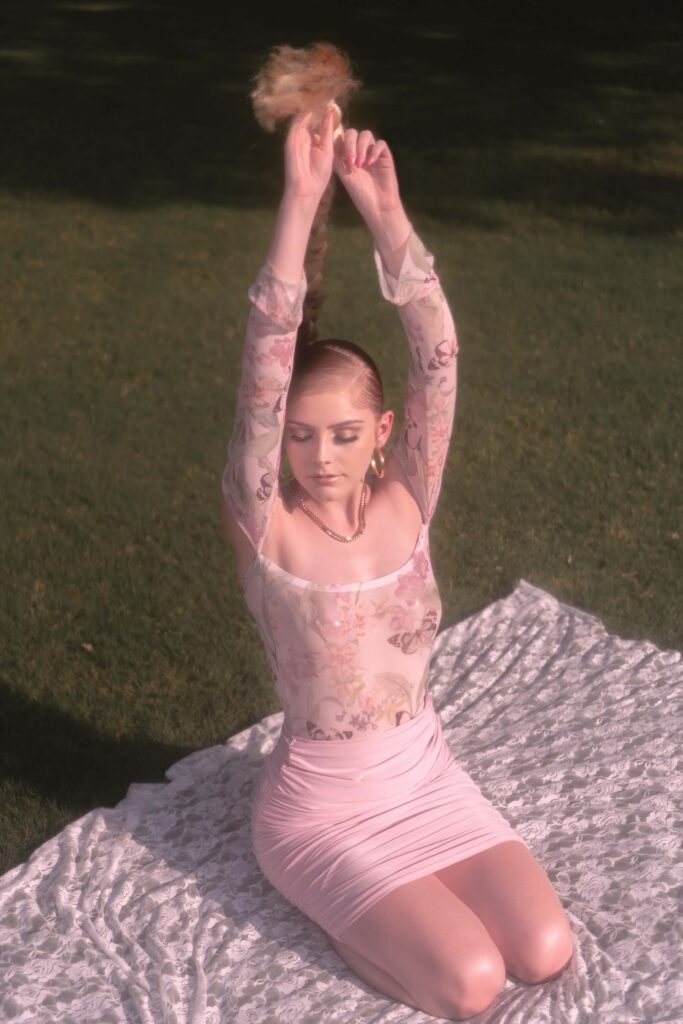 woman kneeling on the grass, hands in the air wearing a pink dress