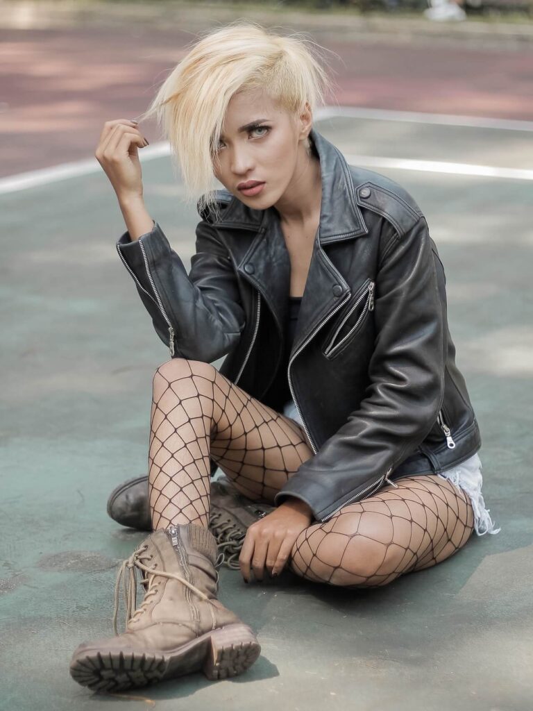 blonde with crazy haircut wearing denim shorts, a leather jacket and fishnets